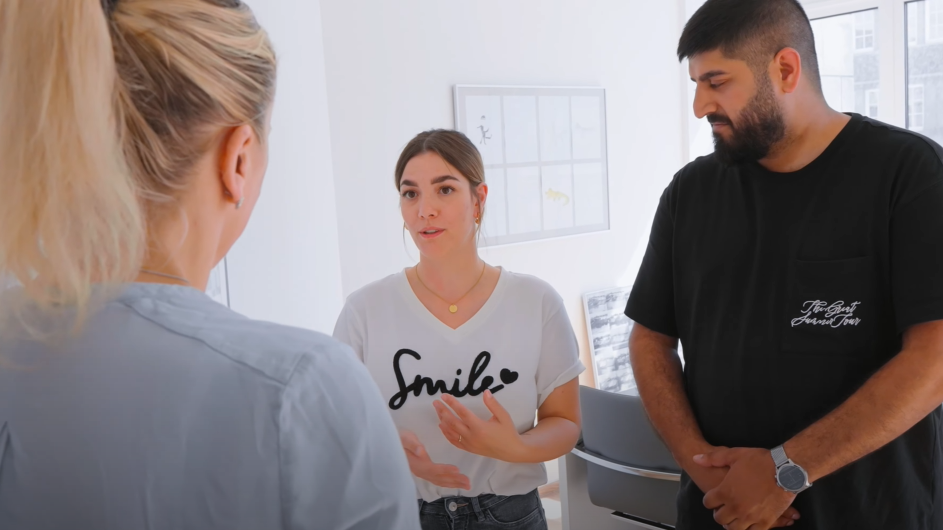 Ein Kinderwunschpaar und eine Ärztin stehen in einem Sprechzimmer. Die Patientin spricht, ihr Partner und ihre Ärztin hören ihr zu.