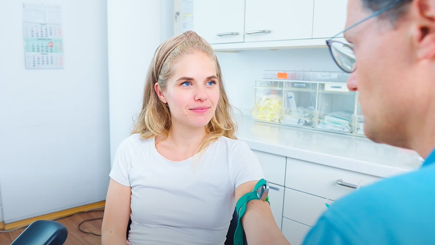 Ein Arzt bereitet seine Patientin für die Blutentnahme vor. Die Patientin hat einen Venenstauer am Oberarm.